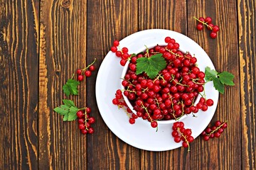 Fresh juicy berries of red currant in a white bowl on a brown wooden background. Harvest red currants.