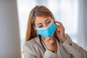 Detail photo of  white woman putting on a blue medical face mask to prevent the flu. Blurred background, focus on the mask. Coronavirus, COVID-19 quarantine. Doctor, nurse concept.
