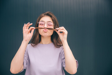 Young stylish trendy woman isolated over grey blue background. Funny playful girl having piece of hair like a moustache. Woman in glasses making funny facial expressions.