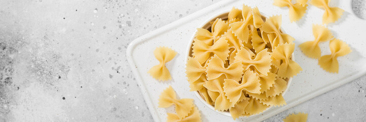 Raw Farfalle pasta in a white bowl on a light gray table. Pasta Farfalle close-up. Banner