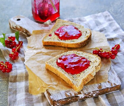 Crispy toast of wheat bread with red currant jam on a wooden board