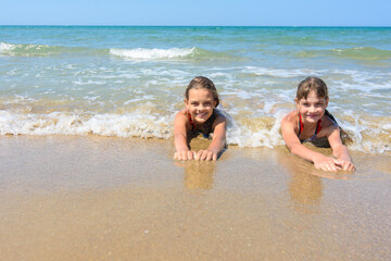 Fototapeta na wymiar Girls lie on the sand of the sea coast and happily look at the frame