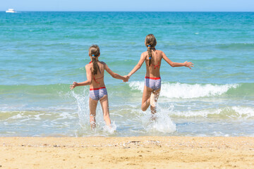Children holding hands run swimming in the sea