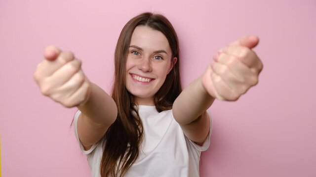 Satisfied lovely young woman stretching hands, looking at camera with amiable friendly smile, wants to embrace, expresses friendly feelings, isolated on pink studio background. Come here into my arms!