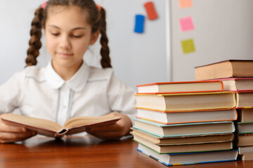 Close up picture of a stack of books on the table with a reading girl on the background. Doing homework, reading literature