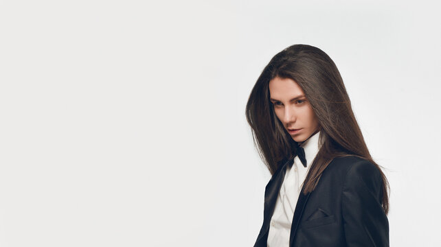 Fashion portrait of androgynous beautiful man with perfect glossy long hair wearing black suit and bow tie. Glamour feminine attractive model with healthy and brown hair. Stylish vogue 