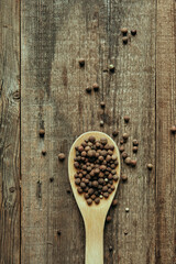 Peas of fragrant pepper in a wooden spoon on an aged wooden table, close up photography for food blog or poster 