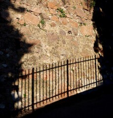 A shadow of a fence cast against an old brown brick wall