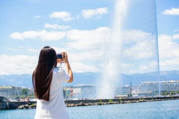 Asian beautiful woman is travel for holiday in the summer of Europe and taking a camera view landscape of lake and bright sky in Geneva Switzerland, copy space.