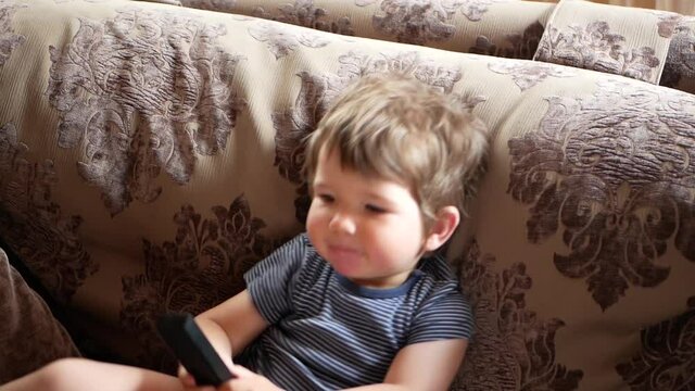 A small child sitting on the sofa, clicks on the TV remote