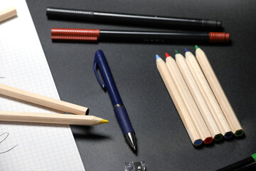 Obraz premium White notebook , color pencils, felt pen and pencil sharpener on a table against black background. Preparing for a school. Back to school.