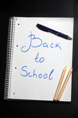 Flat lay view of a white notebook , color pencils, blue pen on a table against black background. Preparing for a school. Back to school.