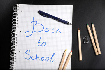 Flat lay view of a white notebook , color pencils, blue pen on a table against black background. Preparing for a school. Back to school.