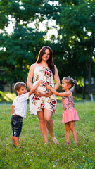 Fototapeta premium Pregnant mother with long hair with two little children posing in the park.