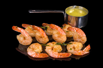 Tasty shrimps with mango or olive oil sauce with reflection, isolated on black background
