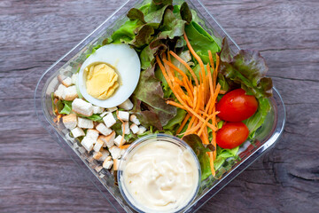 Salad made from fresh vegetables, carrots, tomatoes, chicken eggs, slices of bread and salad dressing packed in a box made of plastic.