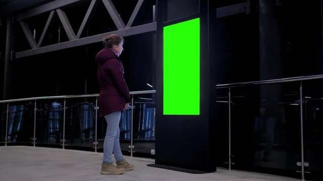 Green screen, mockup, science, copyspace, template, chroma key, technology concept. Woman looking at green display of vertical interactive kiosk at exhibition or museum with low light illumination