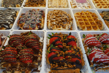 The most delicious Belgian waffles image. Tasty warm waffles covered chocolate with sweet strawberry. Eating them on the city street is touristic lifestyle of big city. High resolution image.