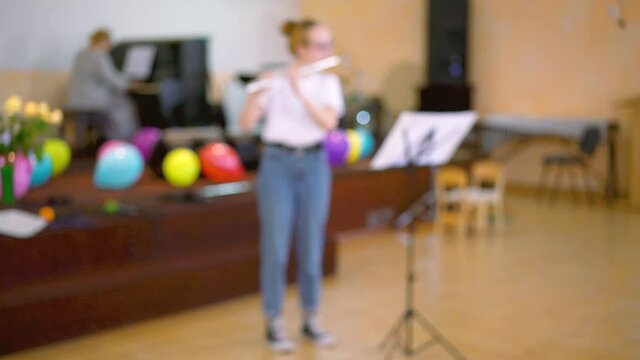 View of girl playing on flute. Teen girl plays the flute in the concert hall. blurry.