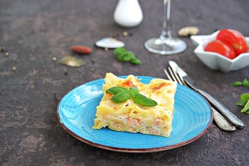 Fish lasagna with salmon and cheese on a blue plate on a dark brown concrete background. Fish and seafood recipes.