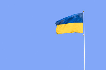 Ukrainian flag flying on a flagpole in against the blue sky. The flag of Ukraine is waving in a wind.