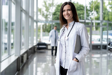 Portrait of young woman doctor with white coat standing in hospital.