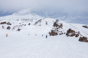 Fototapeta na wymiar Azau glade,Kabardino-Balkar Republic / Russia - 03.13.2016: skiers and snowboarders descend the slope to the foot of mount Elbrus 