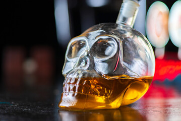 Skull carafe with cognac. Photographed on a bar counter against a dark background.