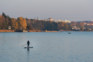 Woman paddleboarding on a lake at seurasaari island in Finland at sunset