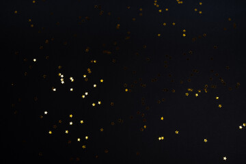 Black contrast color festive background with golden stars glitter confetti. Flat lay style with copy space for text, design. Trendy Holiday concept. Perfect backdrop for social media, blog, postcard