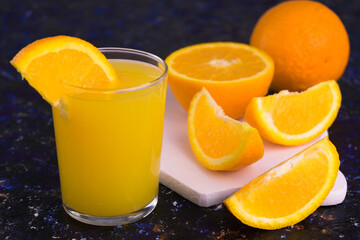 
A glass of organic orange juice and sliced ​​oranges on a dark blue background.