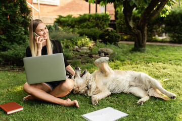 Online learning. Girl with laptop playing with dog Labrador in green park