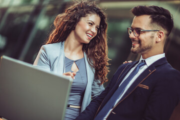 Team of two business people working together outdoors using laptop