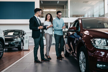 Middle age couple choosing and buying car at car showroom. Car salesman helps them to make right...