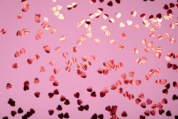 Rose color festive background with red heart shaped confetti. Flat lay style with copy space for text, design. Trendy Valentine's concept. Perfect pink backdrop for social media, blog, postcard.