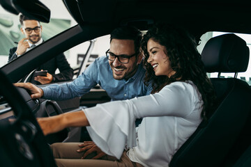 Middle age couple choosing and buying car at car showroom. Car salesman helps them to make right...