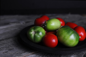 food photography of summer garden organic tomatoes closeup, red and green, on a black wooden plate, front view, against the background of old texture boards, macro photography