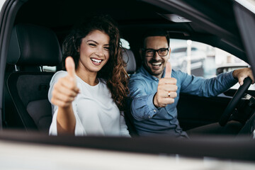 Happy middle age couple enjoying while choosing and buying new car at showroom.