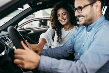 Happy middle age couple enjoying while choosing and buying new car at showroom.