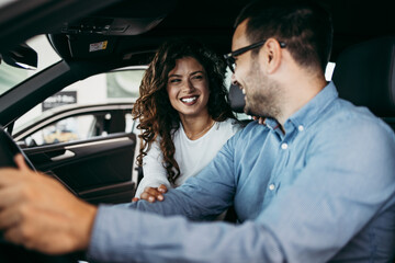 Happy middle age couple enjoying while choosing and buying new car at showroom.