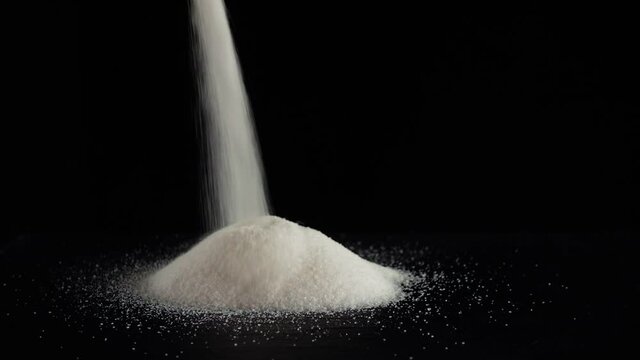 White sugar poured on a table on a black background.
