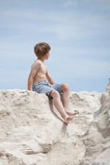 A boy sitting on the sand and looking at the blue sky