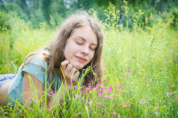 In the summer, a girl lies in a flower meadow.