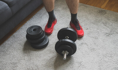 Man standing near adjustable dumbbell with plates at home.
