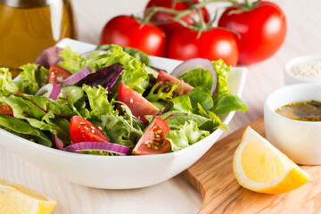 Fresh healthy salad with delicious ruccola, spinach, cabbage, arugula, feta cheese, red onion, cucumber, sesame seeds and cherry tomato on wooden background. Healthy and diet food concept.