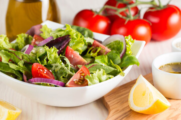 Fresh healthy salad with delicious ruccola, spinach, cabbage, arugula, feta cheese, red onion, cucumber, sesame seeds and cherry tomato on wooden background. Healthy and diet food concept.