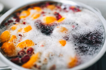 Fresh fruits: apricots, cherries, raspberries, apples are boiled in boiling water in a metal pan on a stove with bubbles and foam close-up. Cooking delicious homemade compote. Photography, concept.