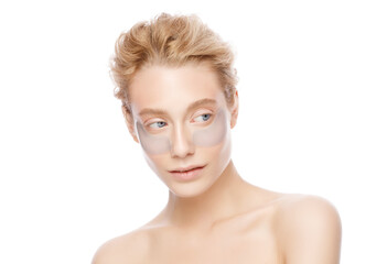 Young beautiful girl standing with naked shoulders, wearing eye patches against dark circles, isolated on white background