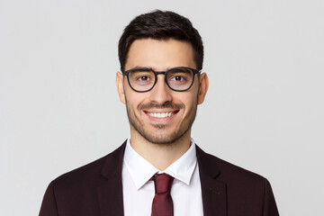 Close up headshot of young businessman wearing glasses and smart casual suit, smiling at camera,...
