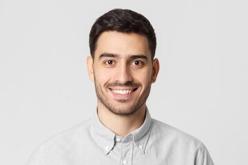 Fototapeta premium Close-up portrait of young smiling handsome man wearing gray shirt, feeling optimistic and confident, isolated on studio background